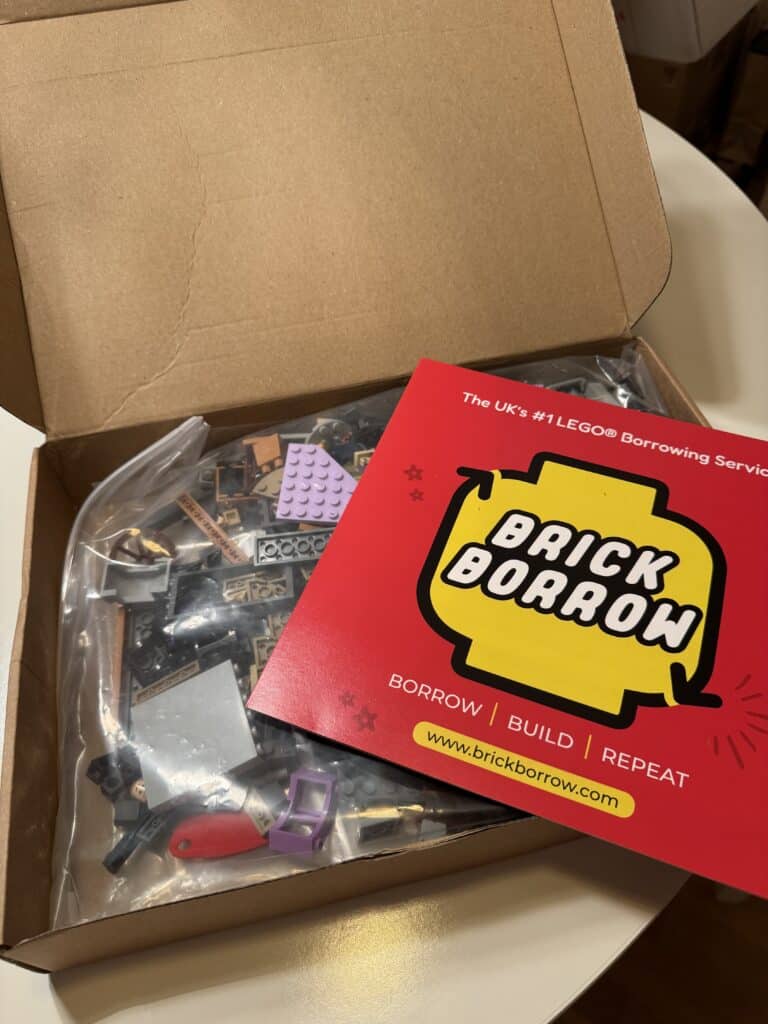 Open cardboard box holding a bag of Lego pieces, with a red Brick Borrow card on top reading 